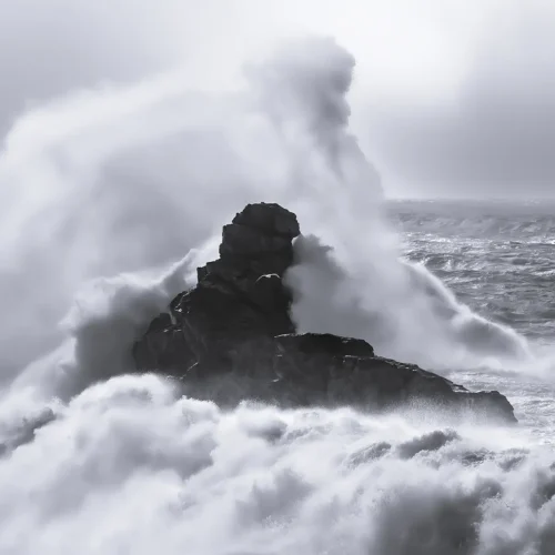 Fotografía en blanco y negro, mar bravío en la costa, una ola enorme sumerge una roca
