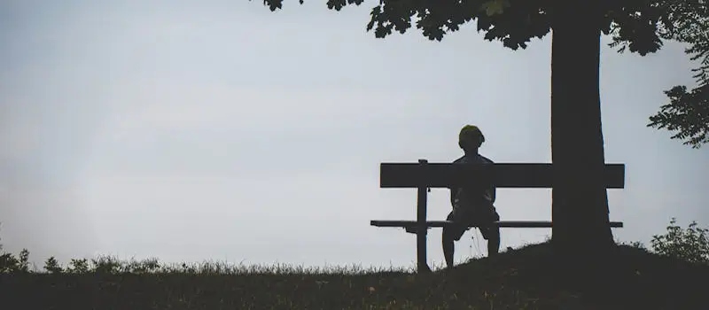 Silhouette d’une personne seule assise sur un banc sous un arbre, ambiance de solitude