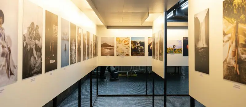Galerie art contemporain avec nombreuses photographies encadrées accrochées sur murs blancs éclairage spot