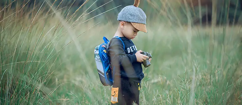 Jeune enfant observant attentivement avec un appareil photo dans une prairie