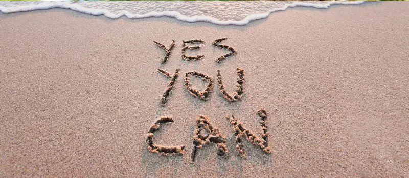 Yes You Can écrit à la main dans le sable humide d'une plage avec vague qui arrive en arrière-plan
