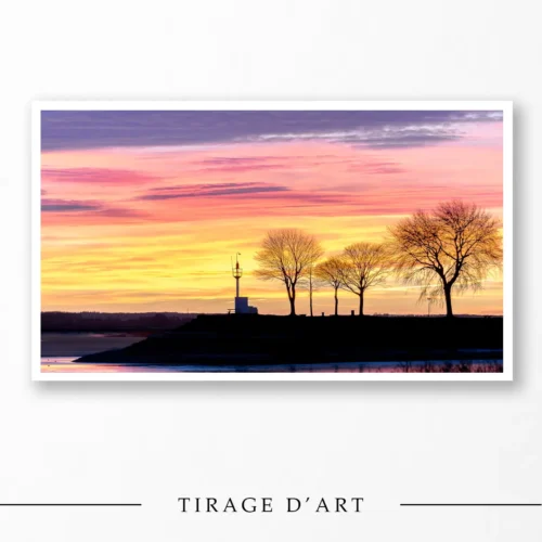 Photograph: Sunrise over the Saint-Valery-sur-Somme lighthouse in the Baie de Somme with trees in silhouette.